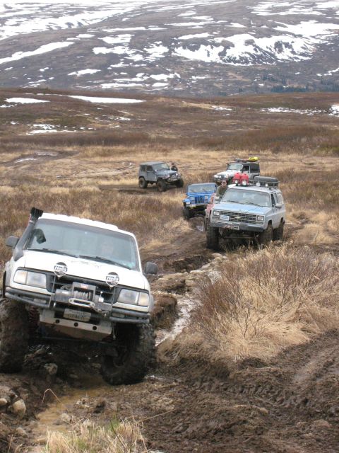 2000 Ford E350 - Multiple off-road vehicles traverse a challenging muddy terrain under a vast, open sky.