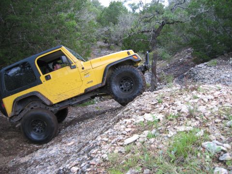 2001 Jeep Wrangler - A yellow Jeep Wrangler navigates a steep, rocky trail surrounded by trees.
