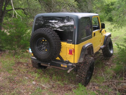 2001 Jeep Wrangler - This yellow 2001 Jeep Wrangler is viewed from the rear, with its spare tire prominently displayed on the back.