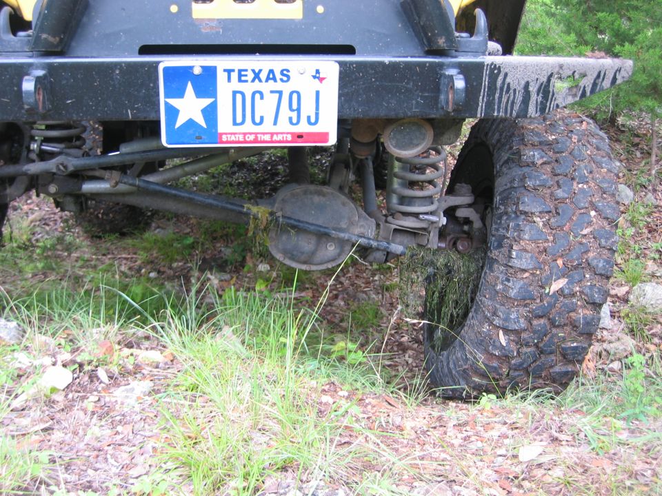 Rear underside of a lifted Jeep showing solid axle, coil springs and muddy off-road tire