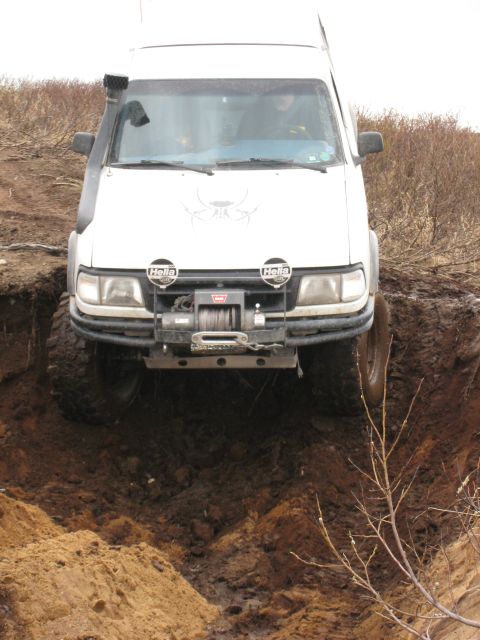 2000 Ford E350 - A white van navigates a muddy ditch, equipped with a snorkel and winch for off-road challenges.