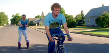 1986 Ford Bronco - One person rides a bicycle while towing another person on roller skates down a residential street.