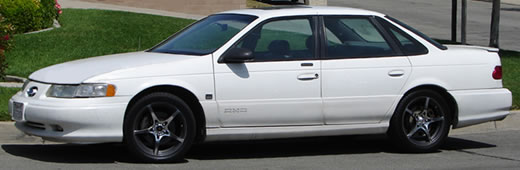 White 1993 Ford Taurus sedan with aftermarket wheels parked on a street