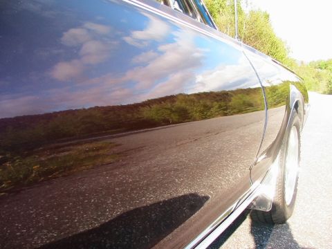 1968 Mercury Cougar - The side of a car is shown with reflections of the sky and landscape on its polished surface.
