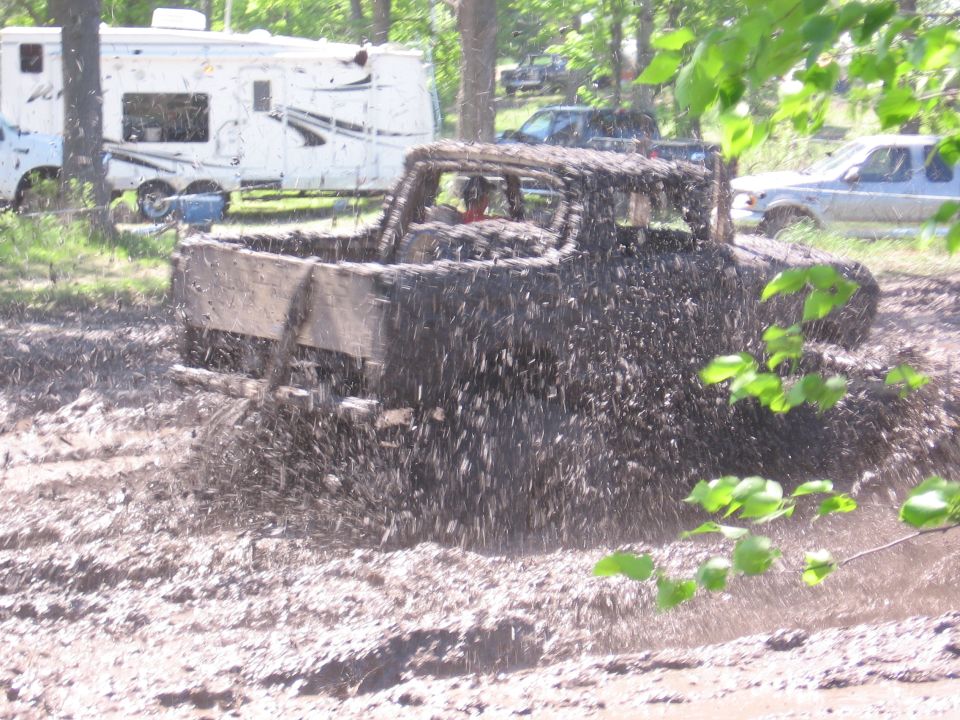 Muddy pickup truck splashing through a mud pit. Camper trailer and other vehicles in background