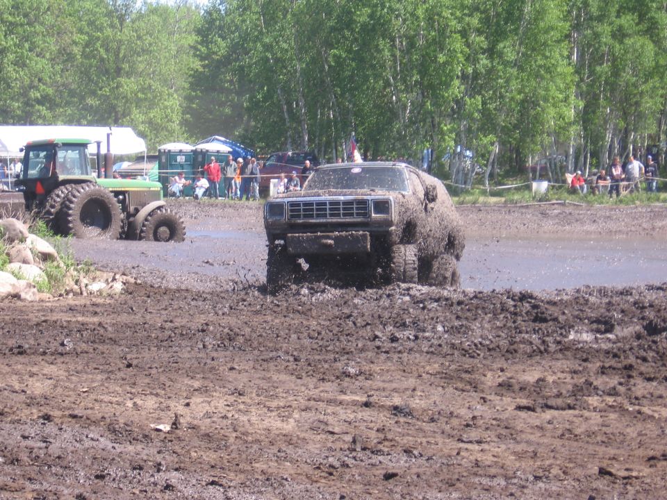 Mud-covered pickup truck with a prominent grille, driving through a mud pit