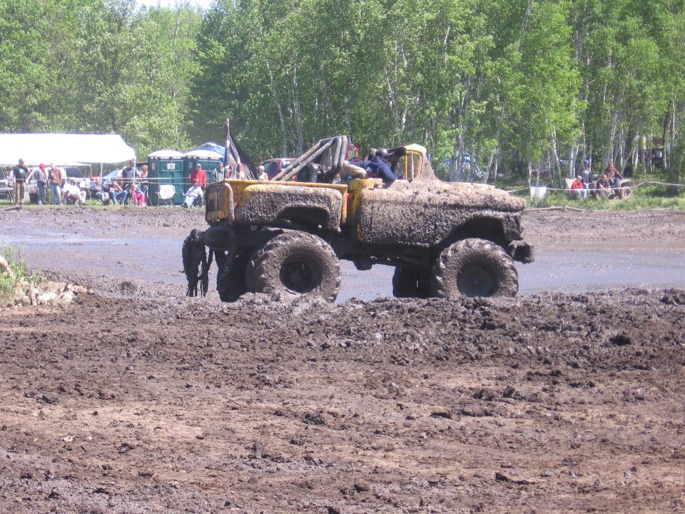 Yellow pickup truck with large tires stuck in mud, people watching in background