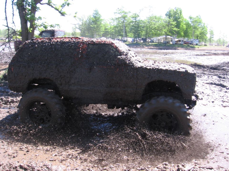 mud-covered SUV driving through a muddy track, splashing water