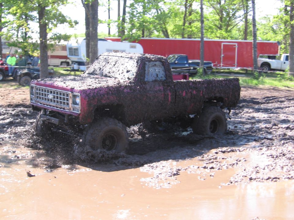 Mud-covered pickup truck with a square grille and rounded fenders, stuck in mud