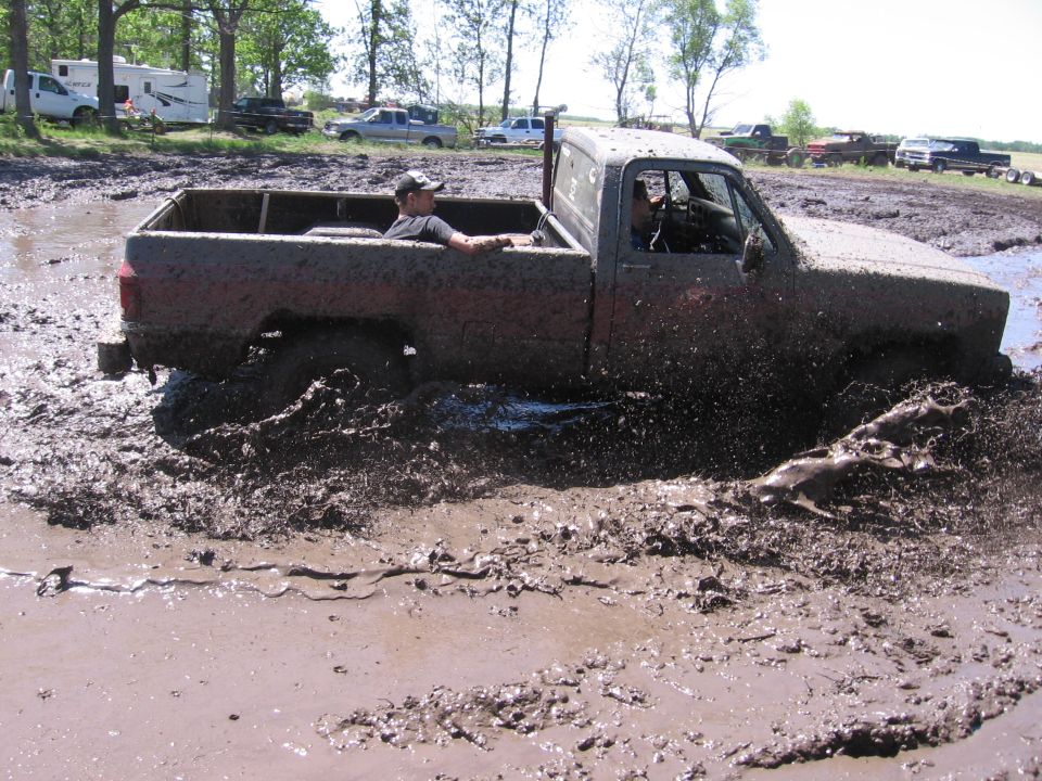 Mud-splattered pickup truck stuck in mud, driver in cab, 1988 model year