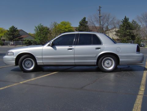 2002 Ford Crown Victoria - A silver 2002 Ford Crown Victoria is shown from the side in a parking lot under a clear blue sky.