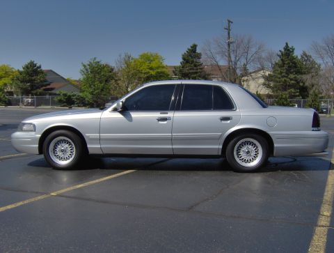 2002 Ford Crown Victoria - A silver 2002 Ford Crown Victoria is parked in an asphalt lot under a clear blue sky.