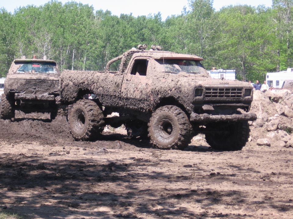Mud-covered Dodge pickup truck with large tires, seen from the front-right