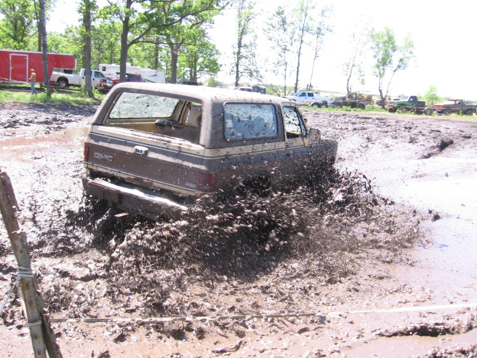Brown GMC Jimmy splashing mud, side view. Watermark 'SUPERMOTORS.NET' visible