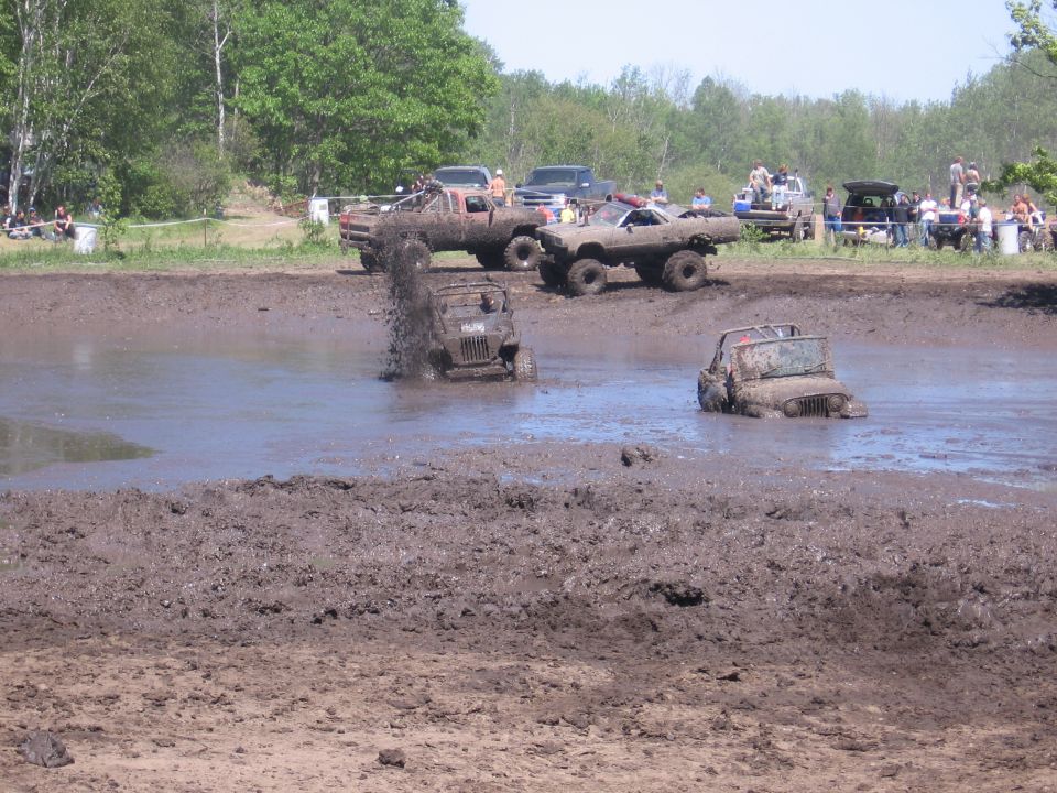 Jeeps and trucks playing in a mud pit with spectators watching