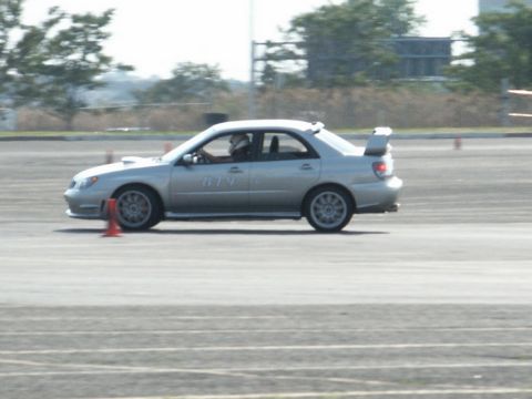 2001 Mercury Grand Marquis - A silver sedan with a prominent rear spoiler navigates a track, indicated by orange cones and a racing number on its door.