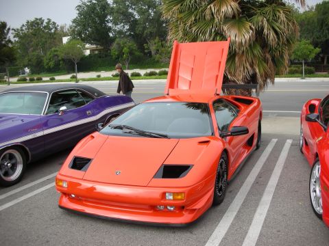 1998 Ford Crown Victoria - An orange Lamborghini Diablo is parked with its hood open, alongside a purple Dodge Challenger and a red sports car.