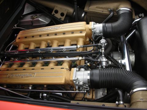 1998 Ford Crown Victoria - The engine bay of a Lamborghini features a prominent gold V12 engine with black intake tubing.