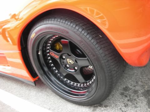 1998 Ford Crown Victoria - Black aftermarket wheel with 'Corse' text and gold emblem on an orange car.