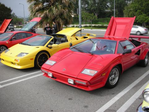1998 Ford Crown Victoria - A red sports car is parked with its engine cover open, alongside other exotic vehicles at a car meet.