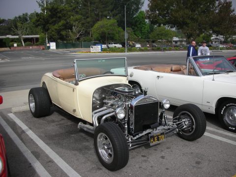 1998 Ford Crown Victoria - A custom hot rod roadster is parked next to a white convertible in a parking lot.