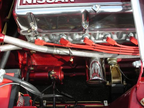 1998 Ford Crown Victoria - Close-up of a polished chrome Nissan engine valve cover with red spark plug wires and braided fuel lines.