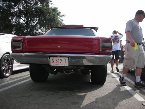 1998 Ford Crown Victoria - A red car with a spoiler and a custom license plate is parked at an outdoor event.