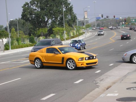 1998 Ford Crown Victoria - A yellow Ford Mustang with black racing stripes drives on a multi-lane road.
