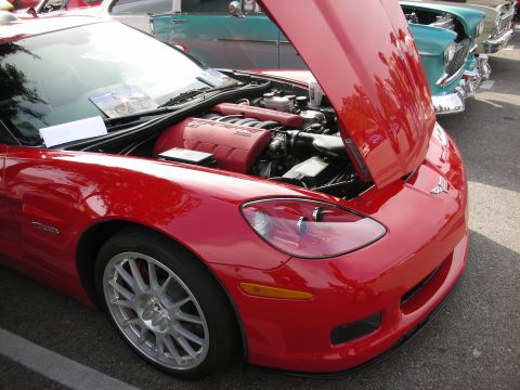 1998 Ford Crown Victoria - A red Chevrolet Corvette with its hood open, displaying the engine and 'CORVETTE Z06' badging, parked at a car meet.