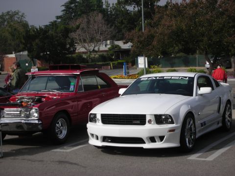 1998 Ford Crown Victoria - Two cars, a white Saleen Mustang and a red Dodge Dart, are parked side-by-side in a lot.