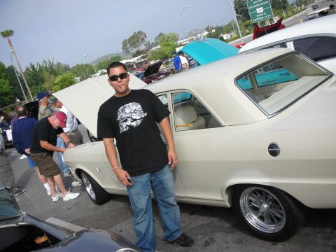1998 Ford Crown Victoria - A man poses next to a classic cream-colored coupe at a car meet, with other vehicles and attendees in the background.