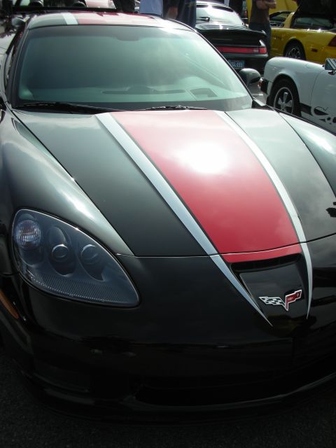 1998 Ford Crown Victoria - Front view of a black Corvette C6 with racing stripes, parked with other cars.