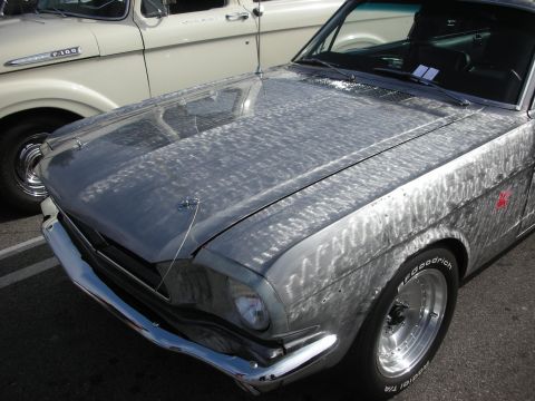 1998 Ford Crown Victoria - A bare metal 1965 Ford Mustang is parked next to a cream-colored truck, its unique finish.