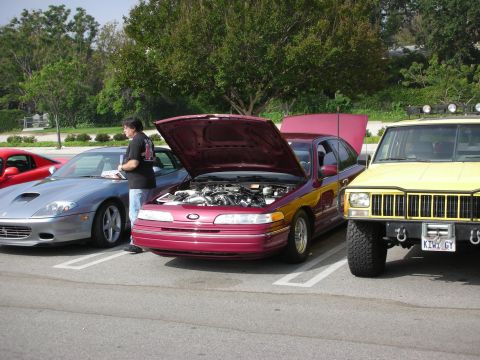 1998 Ford Crown Victoria - A maroon 1998 Ford Crown Victoria is parked with its hood open, alongside other vehicles at an outdoor gathering.