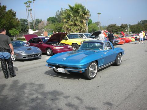 1998 Ford Crown Victoria - Blue 1965 Chevrolet Corvette convertible at a car meet with other vehicles.