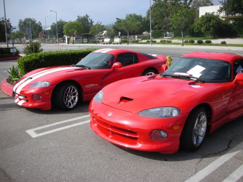 1998 Ford Crown Victoria - Two red sports cars are parked in a lot, one in the foreground and another slightly behind it.