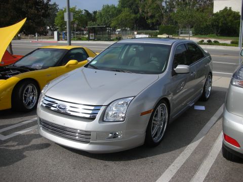 1998 Ford Crown Victoria - A silver Ford Fusion is parked next to a yellow sports car with its hood open.