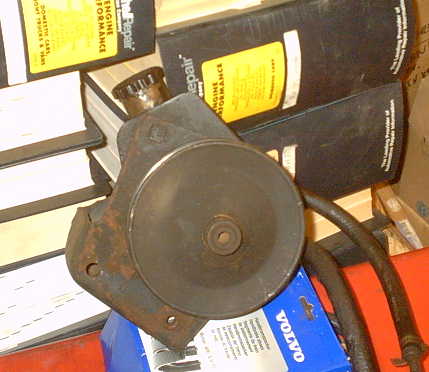1979 Ford Bronco - A close-up of a used power steering pump with hoses, surrounded by automotive repair manuals and a Volvo branded box.
