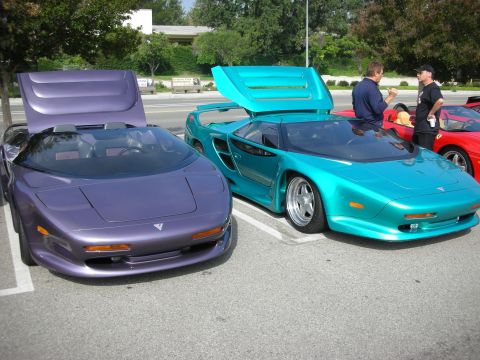 1998 Ford Crown Victoria - Two exotic sports cars, one purple and one teal, are parked side-by-side at an outdoor gathering.