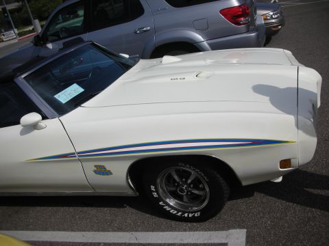 1998 Ford Crown Victoria - A white convertible with colorful racing stripes and "The Judge" badging is parked next to a silver SUV.