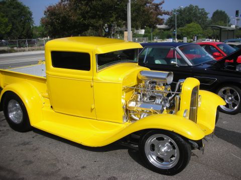 1998 Ford Crown Victoria - A bright yellow hot rod pickup truck is parked next to other vehicles on a sunny day.