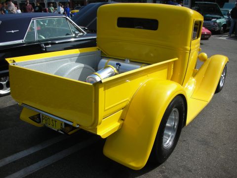 1998 Ford Crown Victoria - A bright yellow pickup truck is parked next to a black car at an outdoor event.