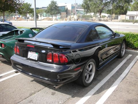 1998 Ford Crown Victoria - A black 1998 Ford Mustang coupe is parked next to a green Lotus Elise.