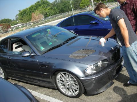 1998 Ford Crown Victoria - A man places a cup on the hood of a gray BMW coupe, with another blue car visible behind it.