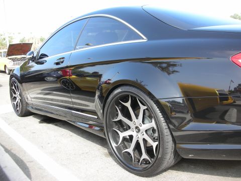 1998 Ford Crown Victoria - A black coupe with aftermarket wheels is parked next to a yellow car with its hood open.