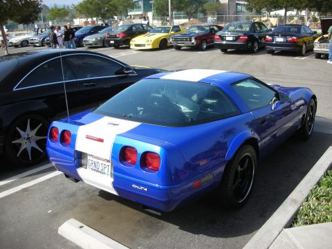 1998 Ford Crown Victoria - A blue and white Chevrolet Corvette is parked in a lot, showing its distinctive rear design and custom racing stripes.