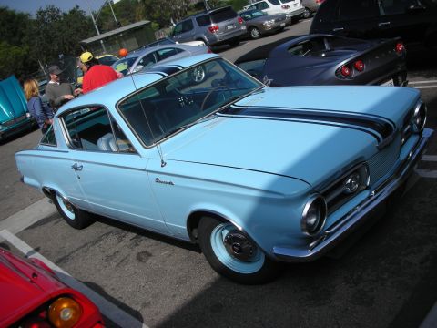1998 Ford Crown Victoria - A light blue 1965 Plymouth Barracuda coupe with black racing stripes is parked at a car meet.