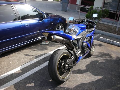 1998 Ford Crown Victoria - A blue motorcycle is parked beside a blue car in a parking lot.