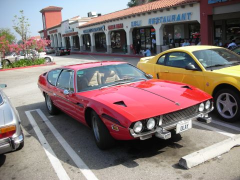 1998 Ford Crown Victoria - Red sports car parked next to a yellow Mustang in a parking lot.