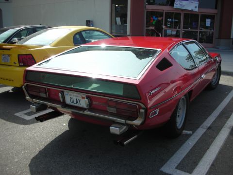 1998 Ford Crown Victoria - A red sports car is parked next to a yellow Ford Mustang in a parking lot.